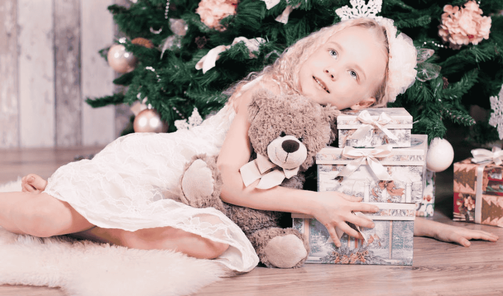 une petite fille sous un sapin de Noël et entouré par les cadeaux