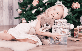 une petite fille sous un sapin de Noël et entouré par les cadeaux