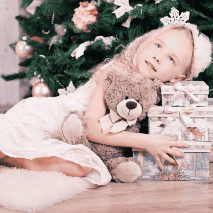 une petite fille sous un sapin de Noël et entouré par les cadeaux