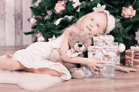 une petite fille sous un sapin de Noël et entouré par les cadeaux