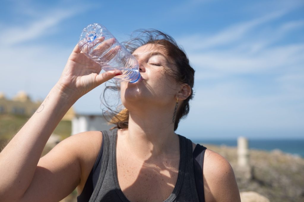 Une femme est en train de boire une bouteille de l'eau pour contre la chaleur